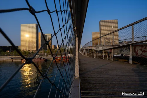 Passerelle Simone-de-Beauvoir et tours de la BnF au soleil levant, à travers un grillage